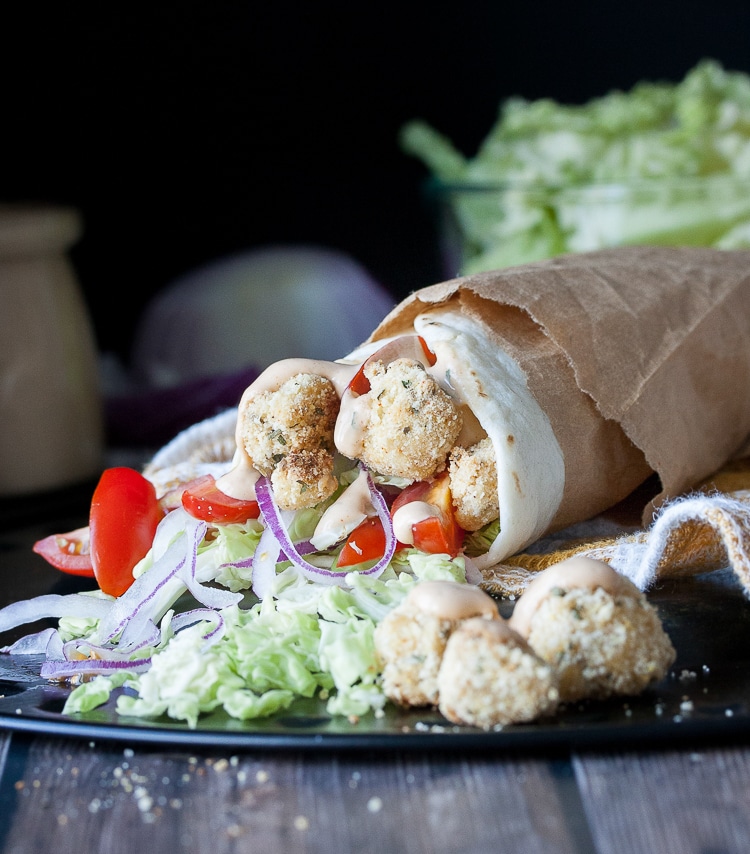 Vegan popcorn cauliflower burrito wrapped in brown paper lying on a plate