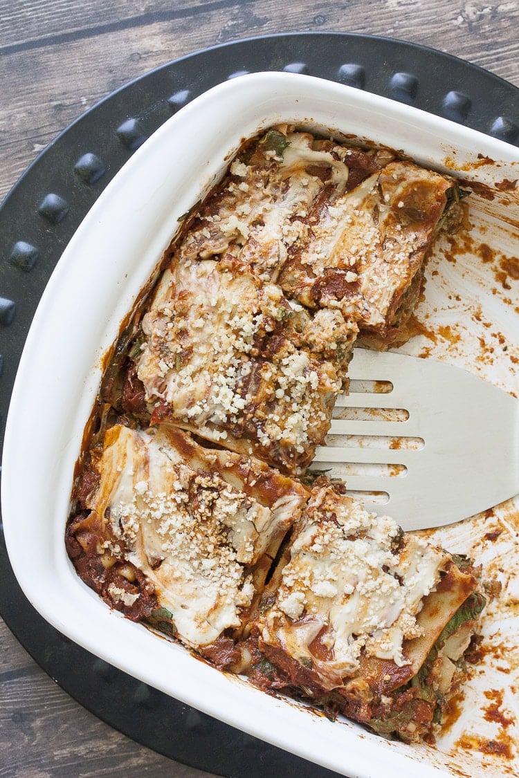 Spatula taking out a piece of vegan creamy pesto and sausage lasagna from a white pan