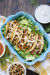 Top view of blue baking pan filled with five buffalo chickpea tacos on a bed of lettuce