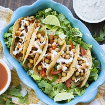 Top view of blue baking pan filled with five buffalo chickpea tacos on a bed of lettuce