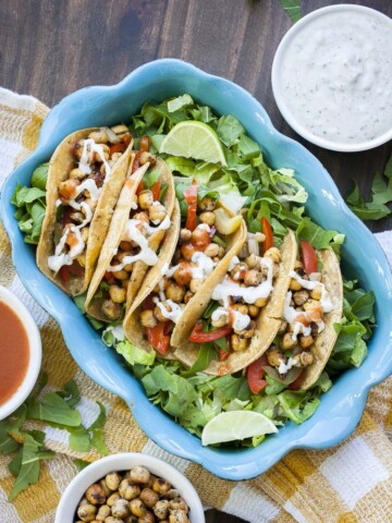 Top view of blue baking pan filled with five buffalo chickpea tacos on a bed of lettuce