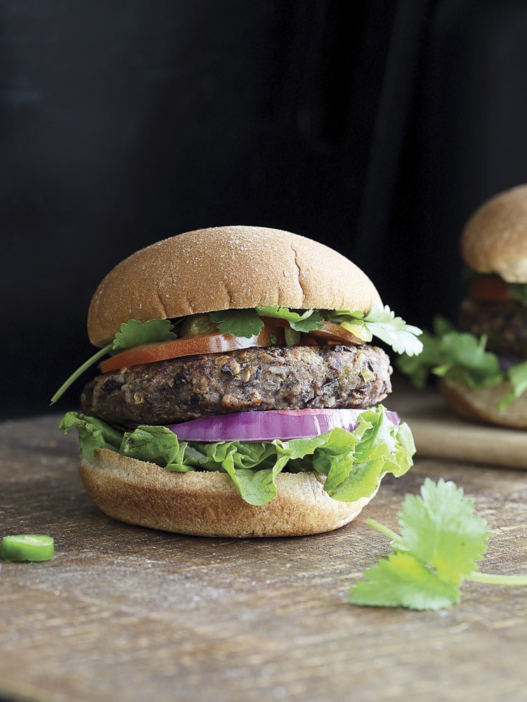 Front view of black bean burger topped with lettuce, onion, tomato and cilantro