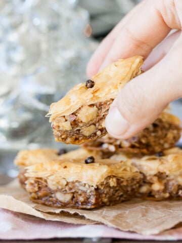 Hand grabbing a piece of Greek vegan baklava off of a stack of baklava