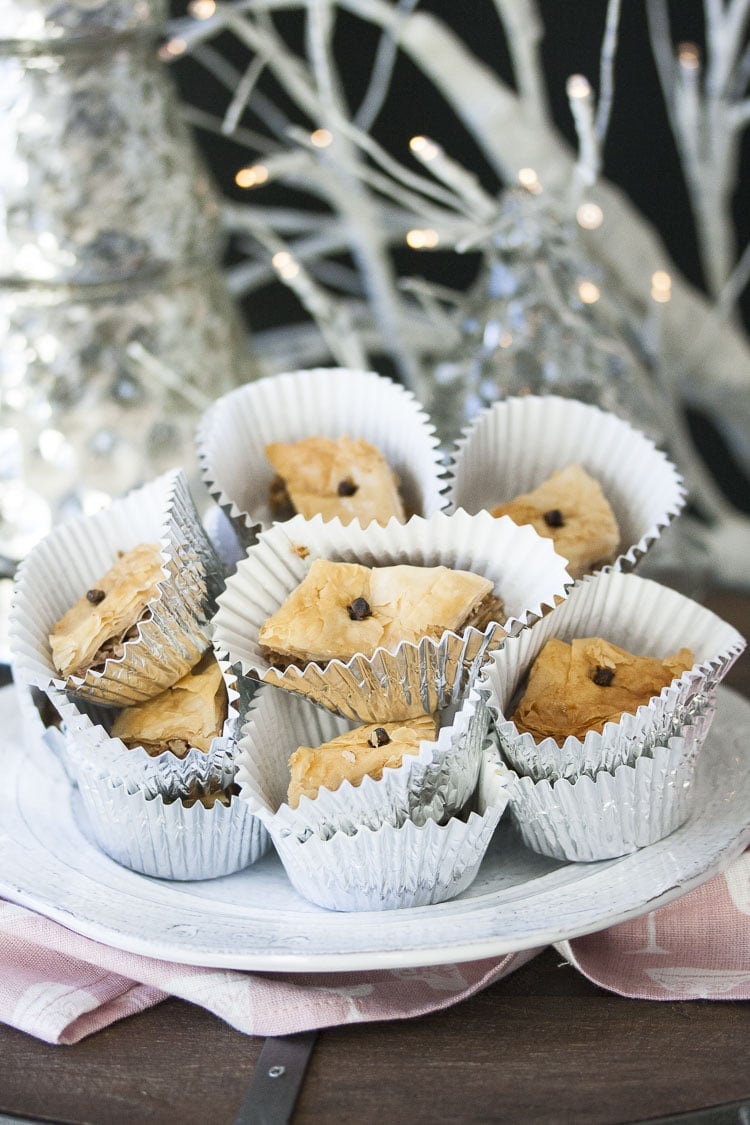 A stack of pieces of baklava in foil baking cups on a white plate