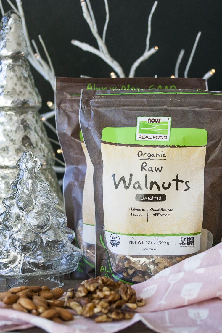 Two packages of NOW Foods walnuts and almonds surrounded by winter holiday decor