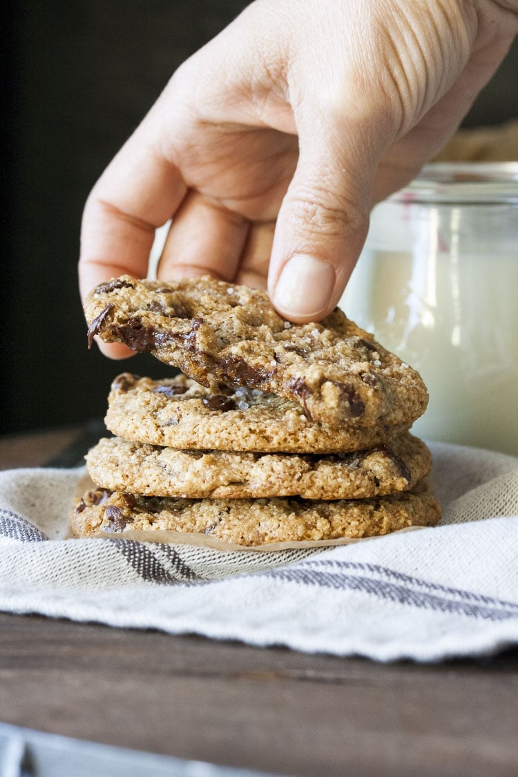 Hand grabbing top half eaten sea salt chocolate chip cookie from a pile