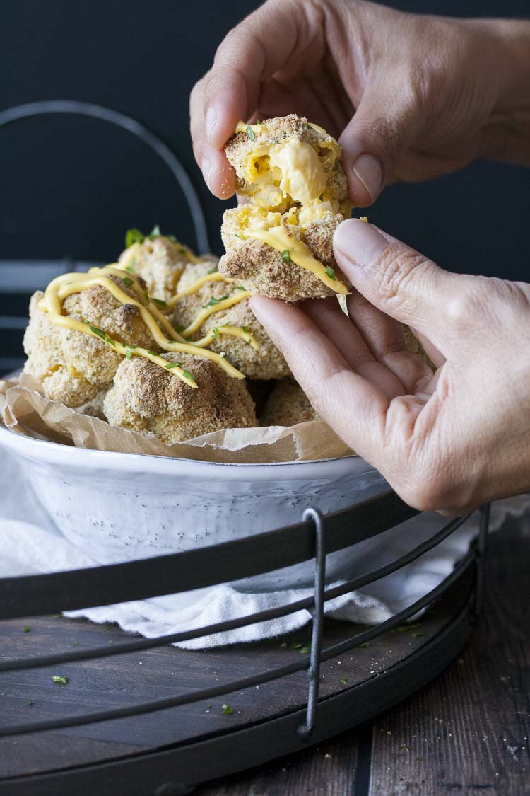 Hand tearing open a crispy baked mac and cheese ball to reveal the cheesiness inside