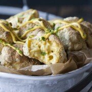 Crispy baked mac and cheese balls, one half eaten, piled in a white bowl