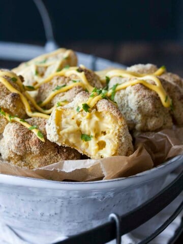 Crispy baked mac and cheese balls, one half eaten, piled in a white bowl