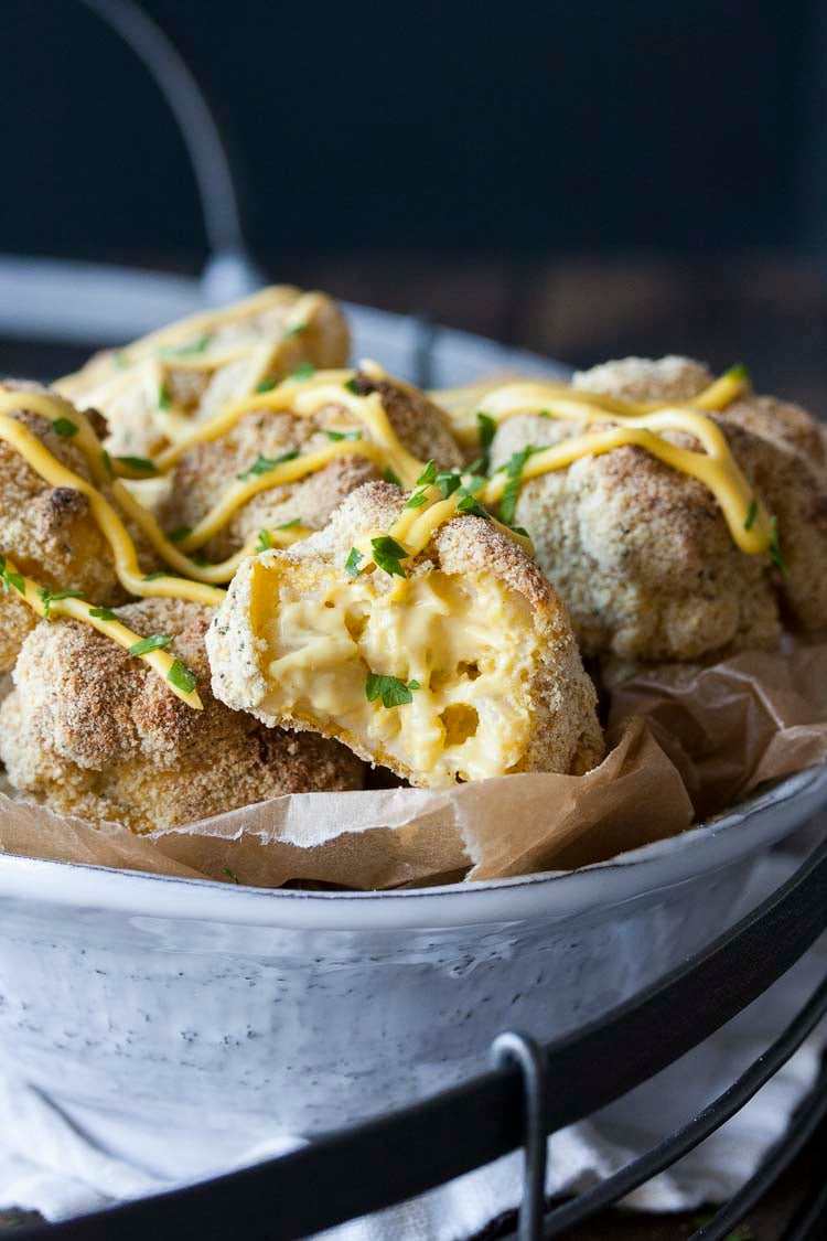 Crispy baked mac and cheese balls, one half eaten, piled in a white bowl