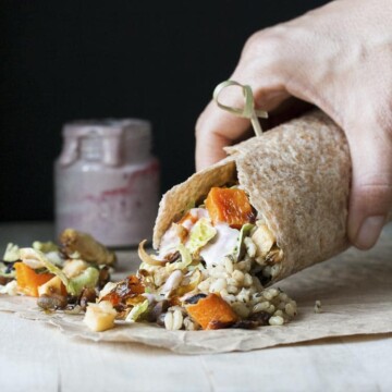 Hand holding burrito filed with roasted fall vegetables, rice and vegan mayo