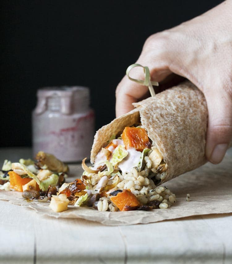 Hand holding burrito filed with roasted fall vegetables, rice and vegan mayo