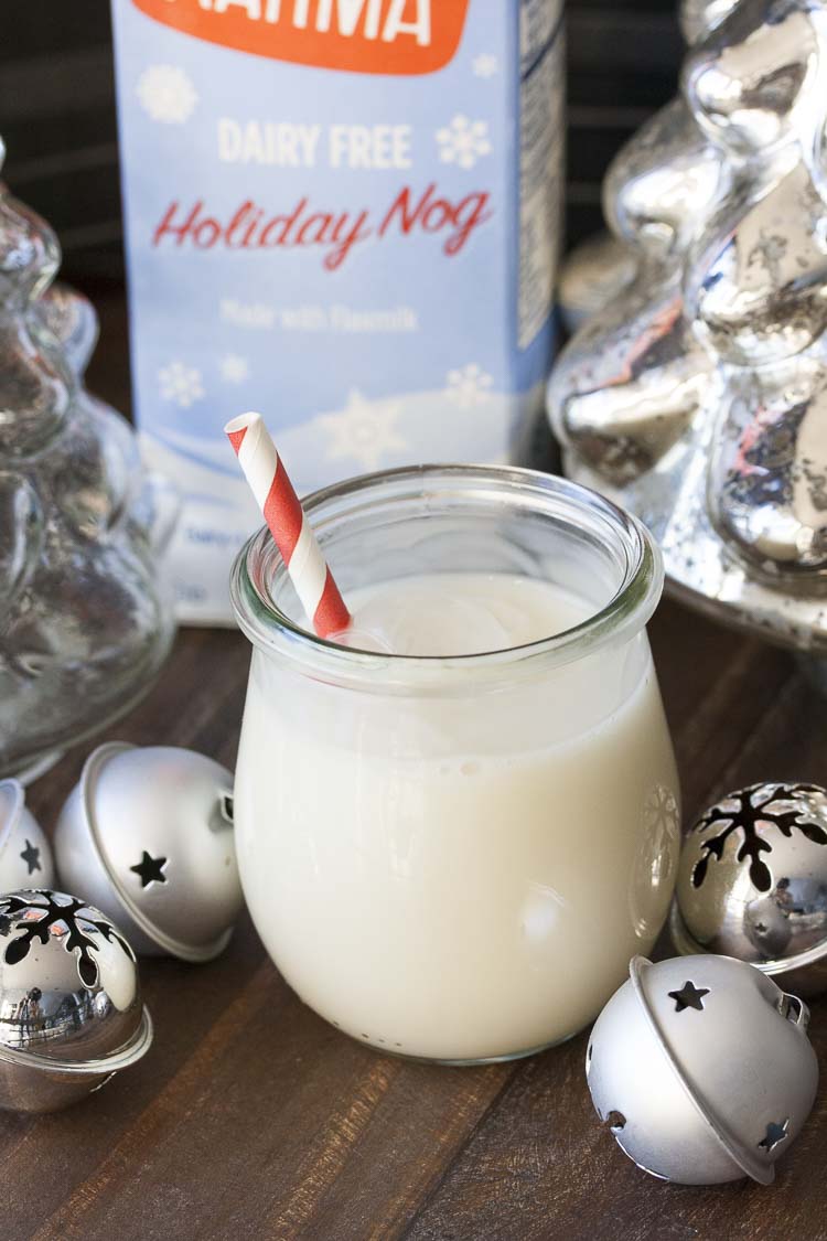 Glass jar of egg nog with a striped red straw surrounded by Christmas decorations