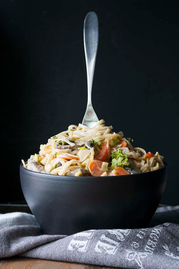 Black bowl with a fork standing up in the middle of peanut noodles and veggies