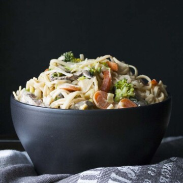 Black bowl filled with noodles and veggies covered in peanut sauce