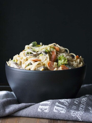 Black bowl filled with noodles and veggies covered in peanut sauce