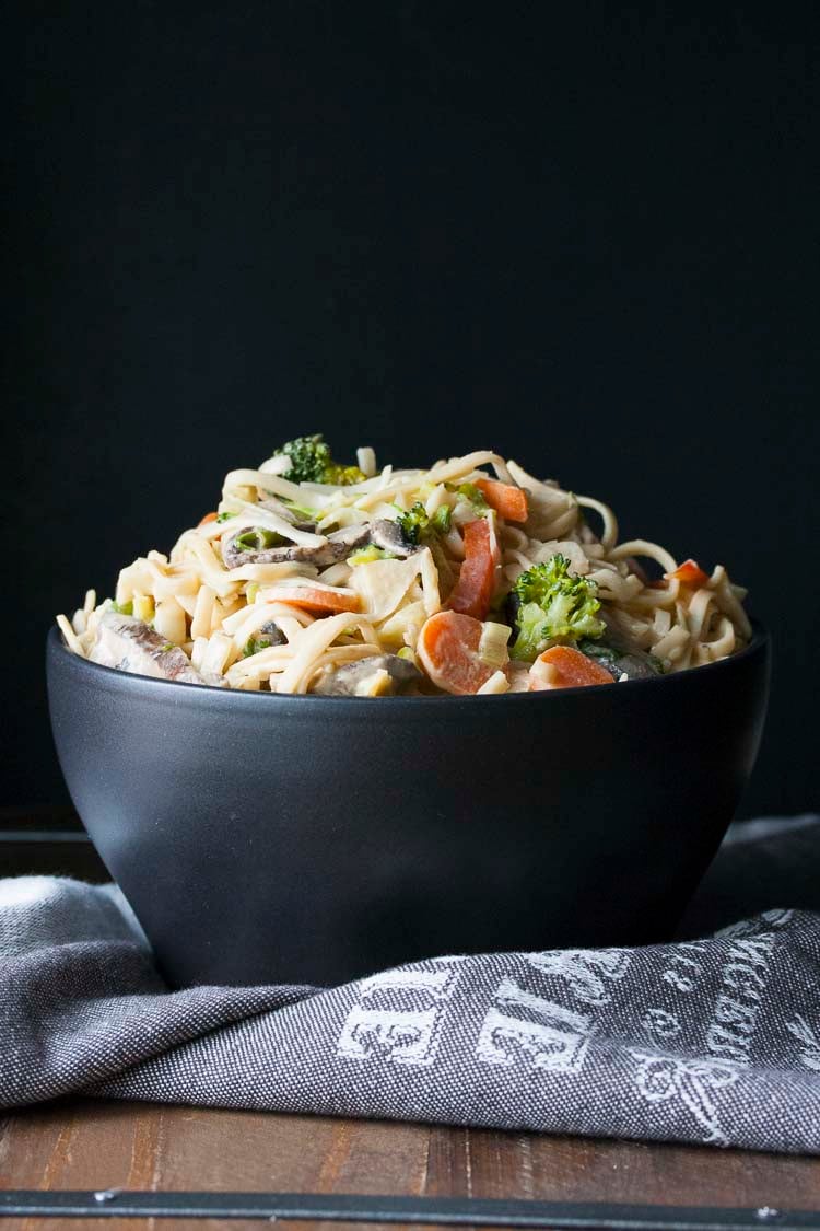 Black bowl filled with noodles and veggies covered in peanut sauce