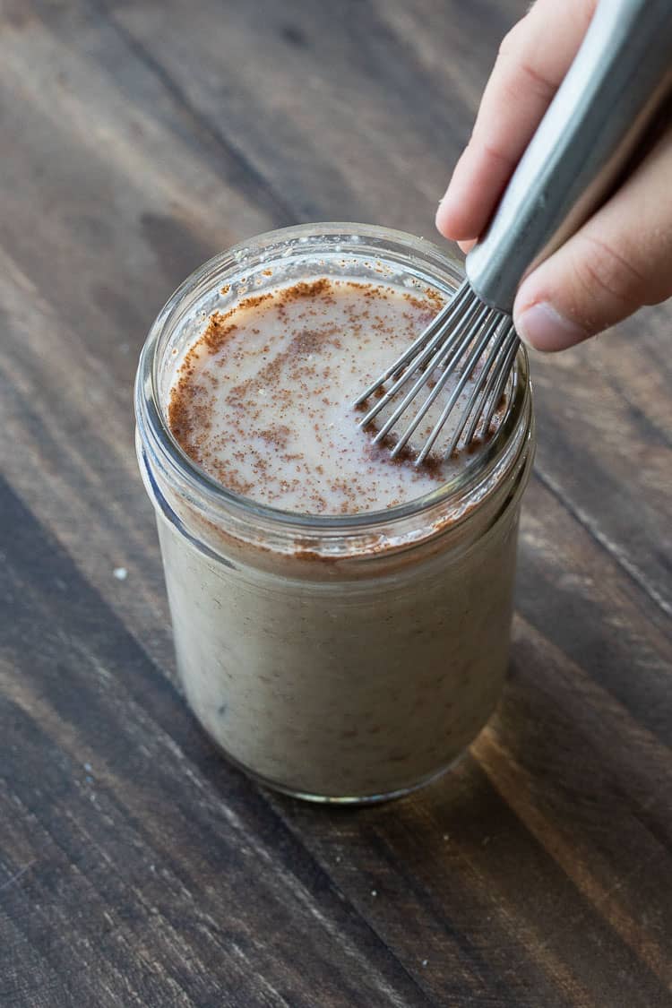 Hand whisking a light brown liquid in a glass jar