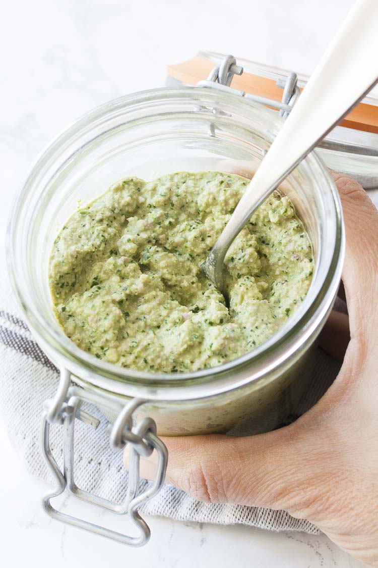 Hand holding glass jar filled with vegan spinach nut based ricotta