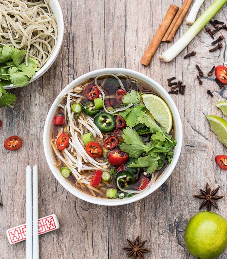 Top view of bowl of veggie Pho soup with red and green hot peppers and noodles