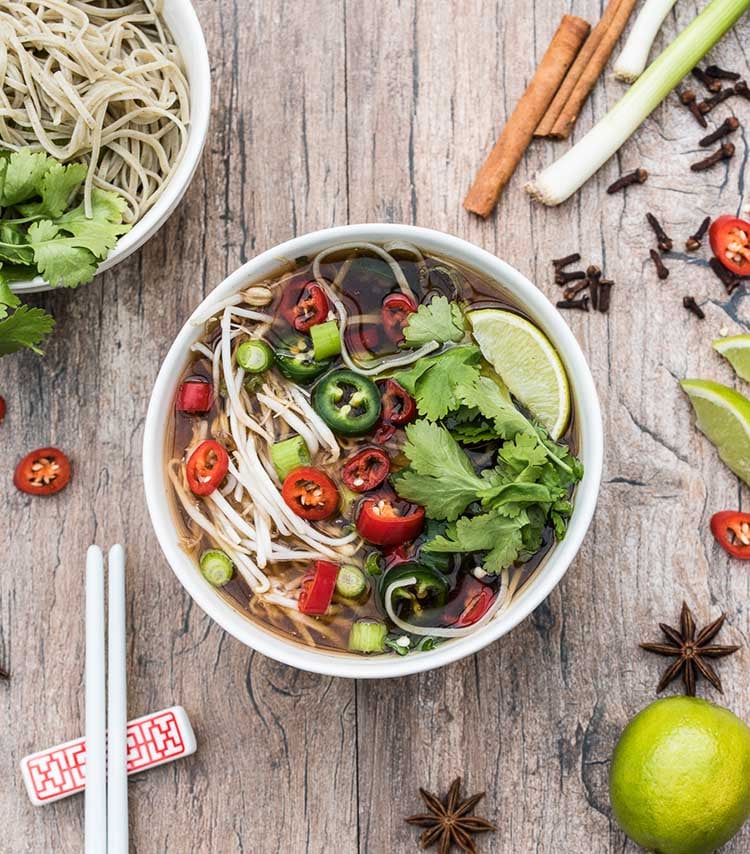 Top view of bowl of veggie Pho soup with red and green hot peppers and noodles