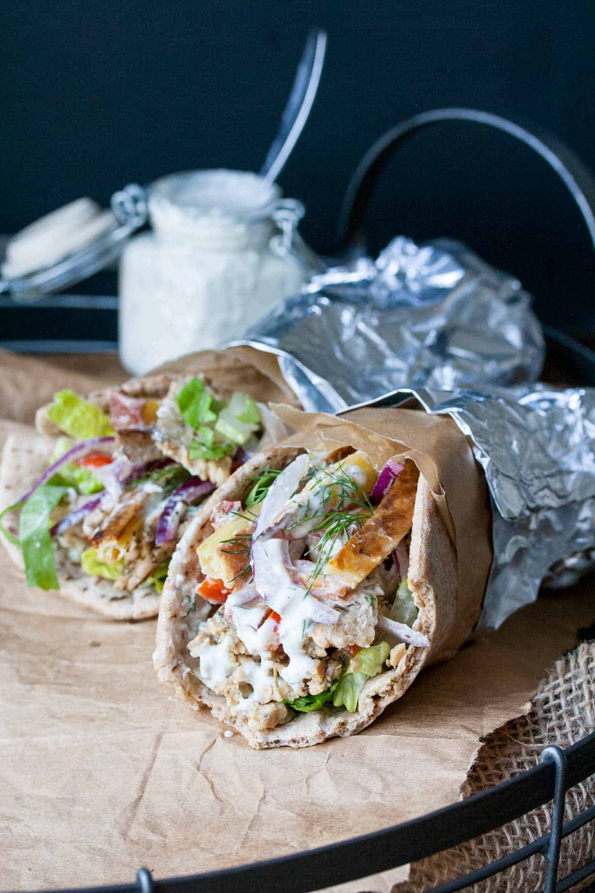 Two tempeh Greek gyros filled with veggies and tzatziki sauce and wrapped in foil