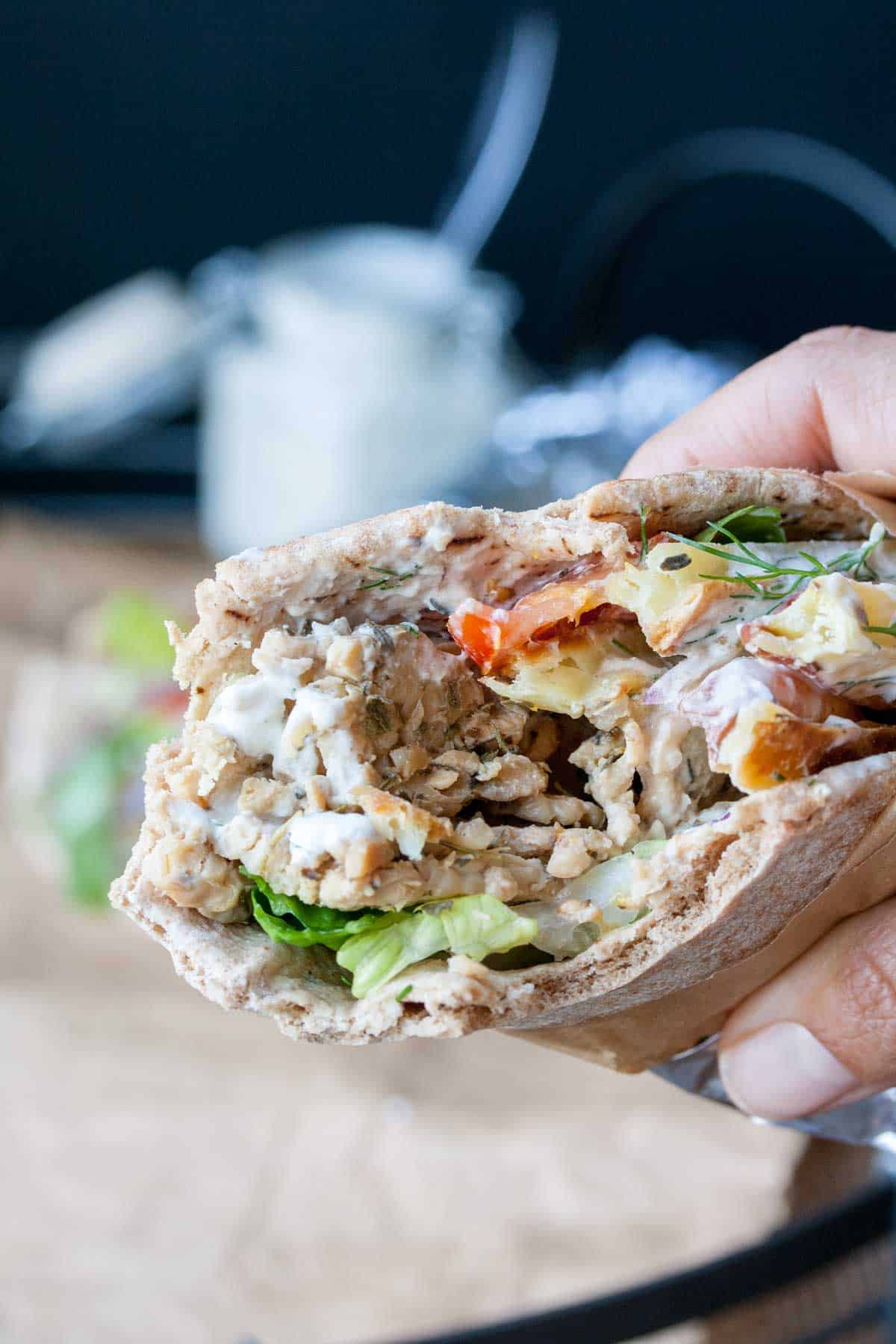 A hand holding a gryo wrap filled with tempeh and veggies and a bite out of it.