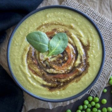 Top view of creamy spinach pea soup in a black bowl next to a few green peas