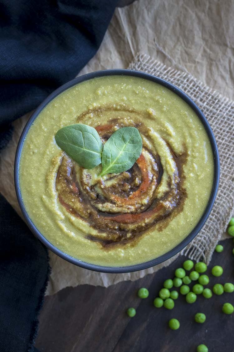 Top view of creamy spinach pea soup in a black bowl next to a few green peas