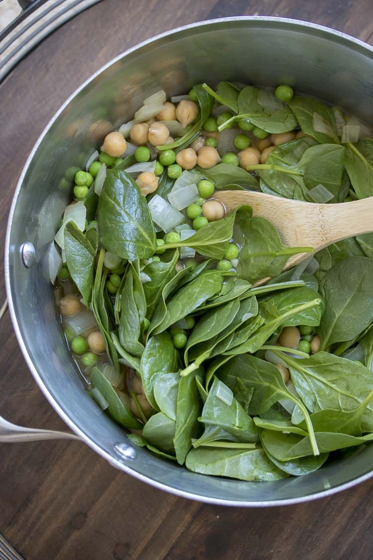 Top view of wooden spoon mixing spinach and peas in stainless steel pot