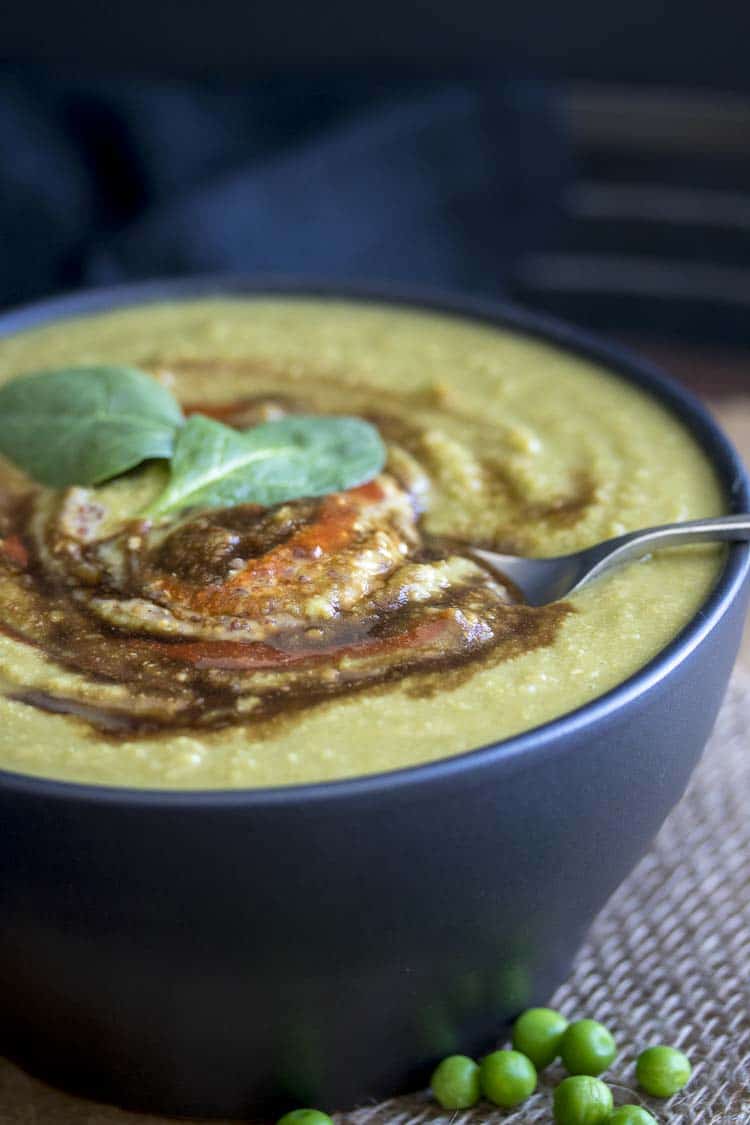 Front view of spoon dipping in bowl of creamy spinach pea soup