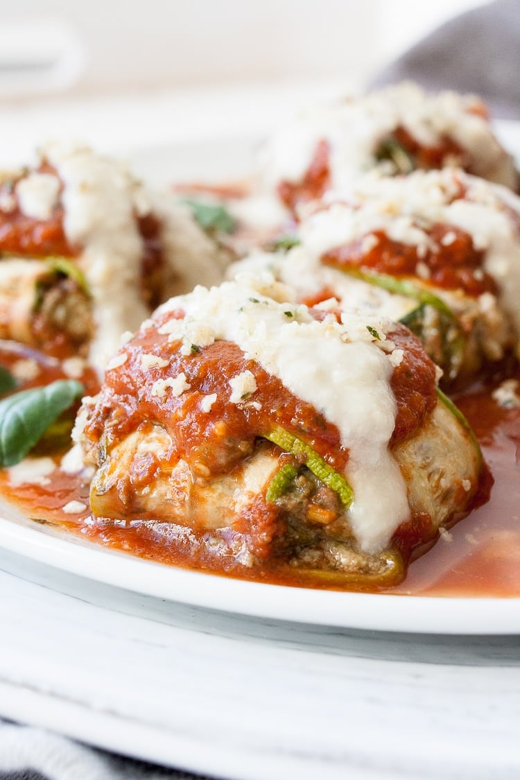 Zucchini ravioli covered in red and white sauce on a while plate.