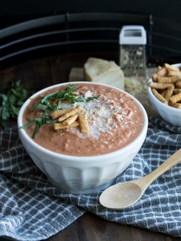 White bowl filled with vegan tomato bisque on a grey towel with white squares.