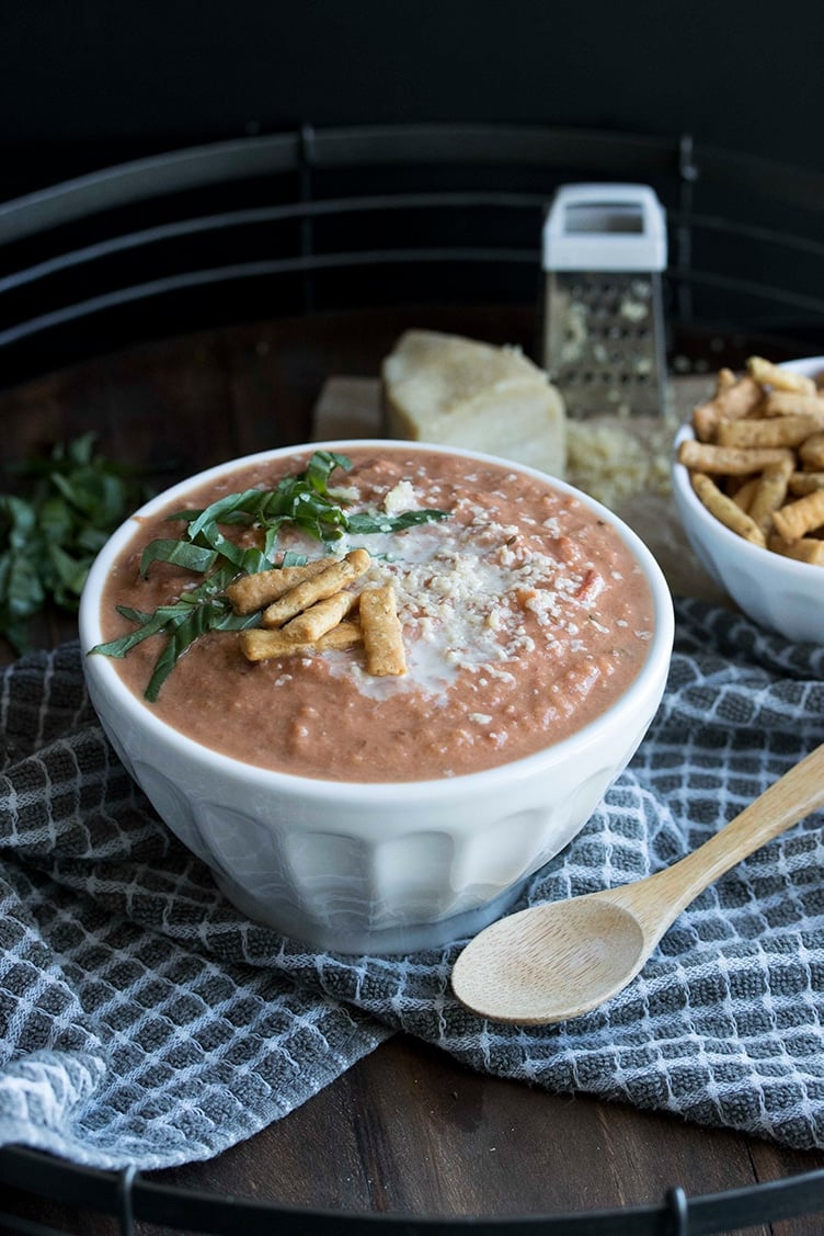 White bowl filled with vegan tomato bisque on a grey towel with white squares.