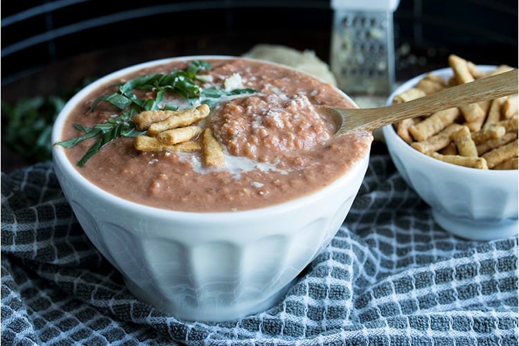 Wooden spoon scooping out a bite of chunky tomato bisque from a white bowl.