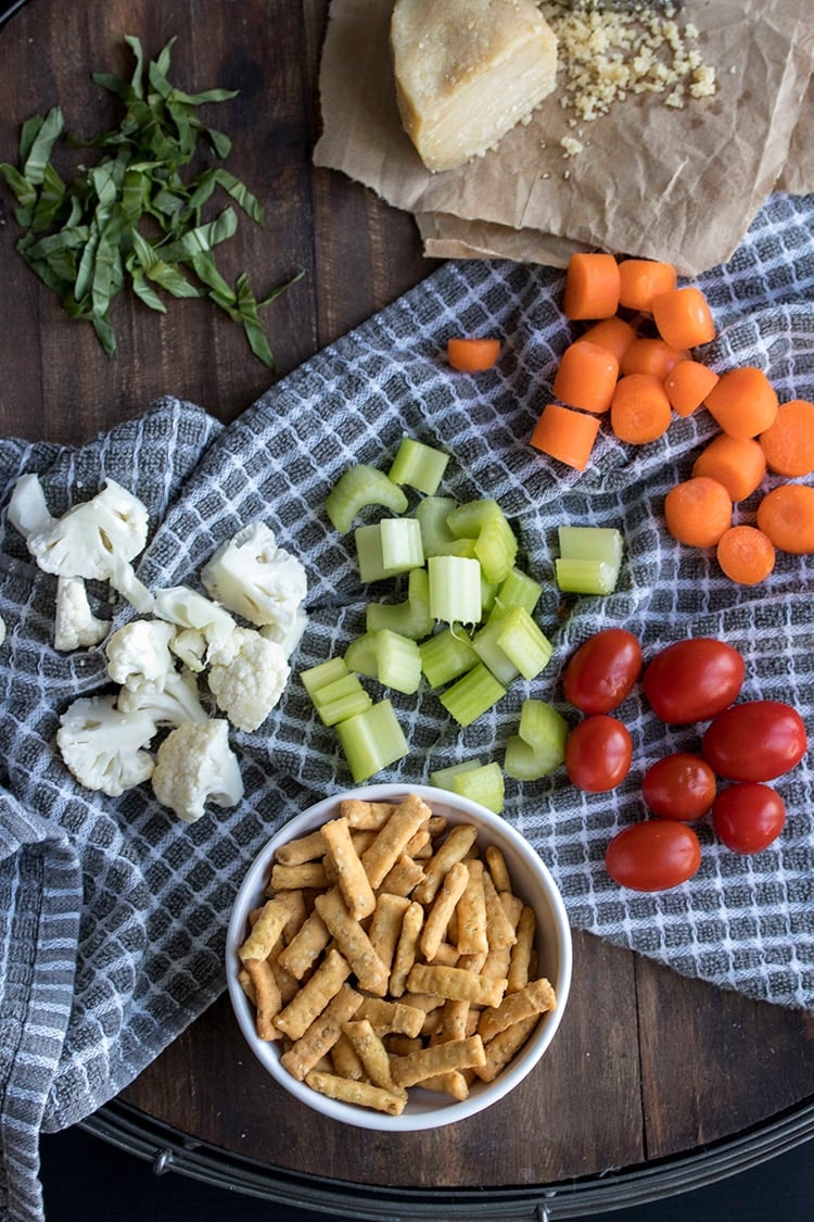 Top view of piles of chopped cauliflower, celery, carrots and tomatoes on a grey and white towel