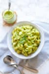 Top down view of a white bowl with green mac and cheese in it and a striped towel under.