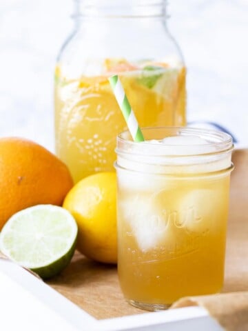 White tray with sparkling citrus tea over ice next to citrus fruit