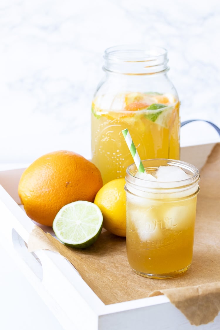 Glass pitcher with sparkling citrus tea next to glass of tea and citrus fruit