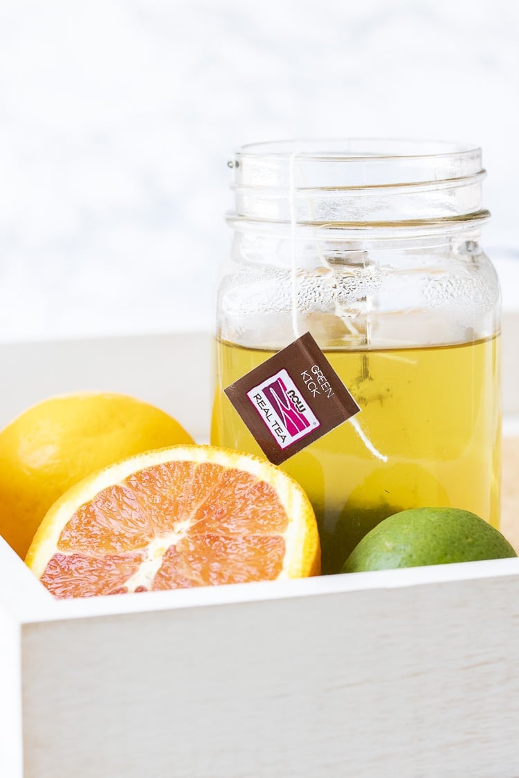 White tray with citrus fruit and glass mug of brewing green tea