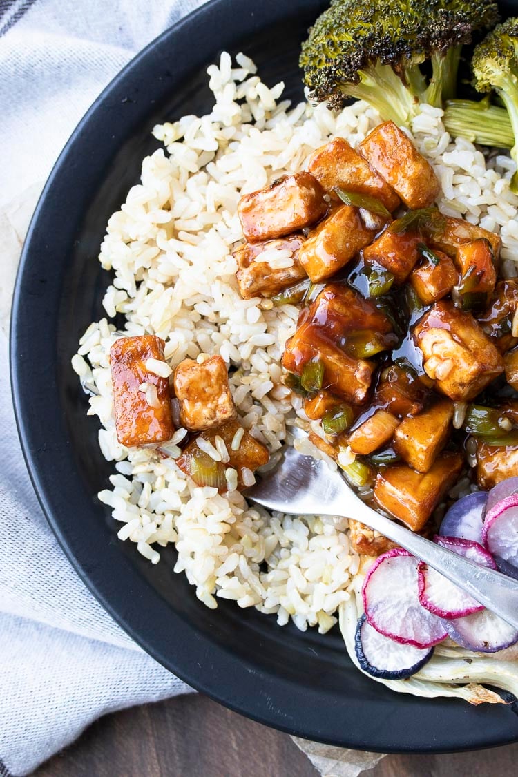 Close up of fork in brown rice with General Tso's tofu