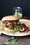 Vegan pulled pork sandwich with mushrooms topped with arugula, pickles and tomatoes
