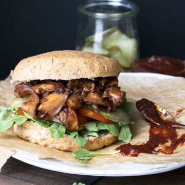 Vegan pulled pork sandwich with mushrooms topped with arugula, pickles and tomatoes