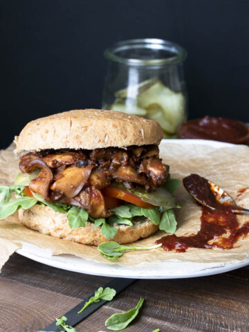 Vegan pulled pork sandwich with mushrooms topped with arugula, pickles and tomatoes