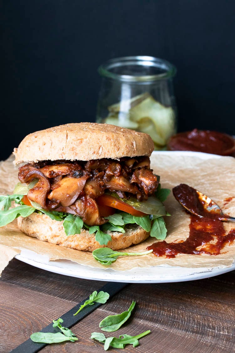 Vegan pulled pork sandwich with mushrooms topped with arugula, pickles and tomatoes