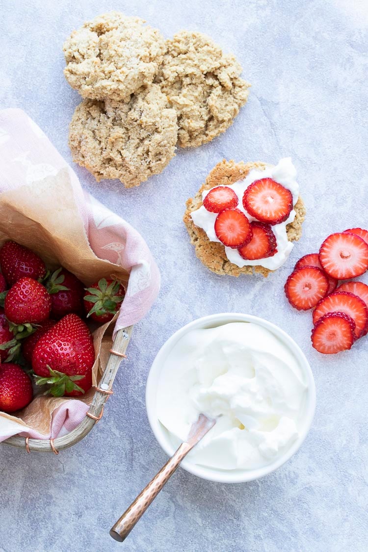 Top view of strawberries, whipped cream, biscuits and partially assembled strawberry shortcake