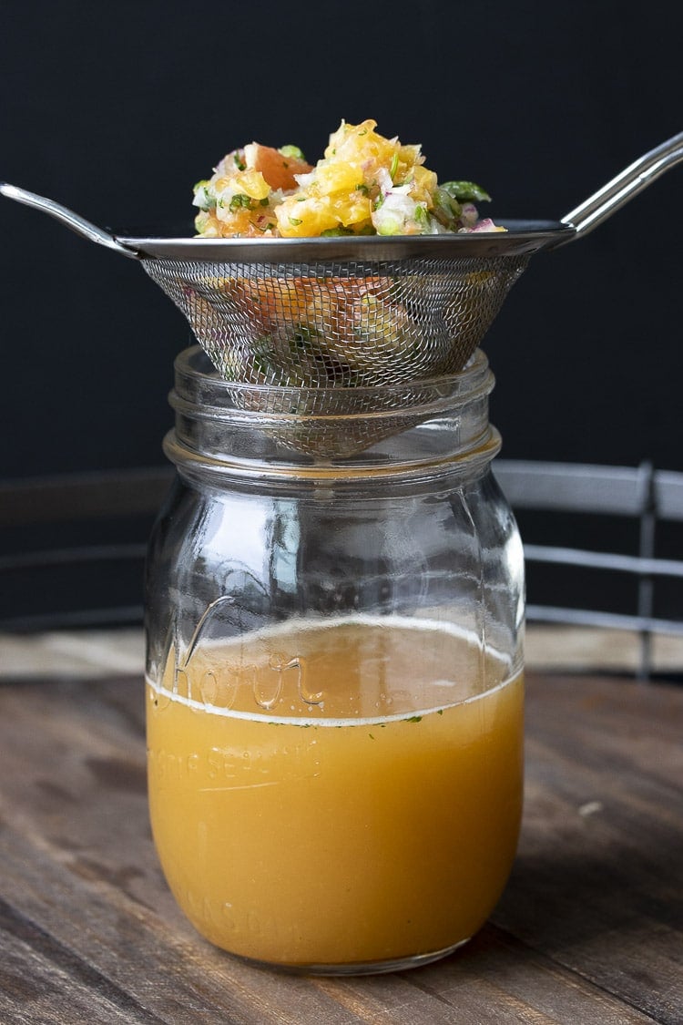 Sieve with citrus salsa draining it's juice into a glass jar