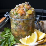 Glass jar of fresh citrus salsa on a wooden tray next to cilantro and orange slices