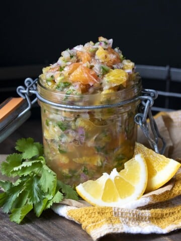 Glass jar of fresh citrus salsa on a wooden tray next to cilantro and orange slices