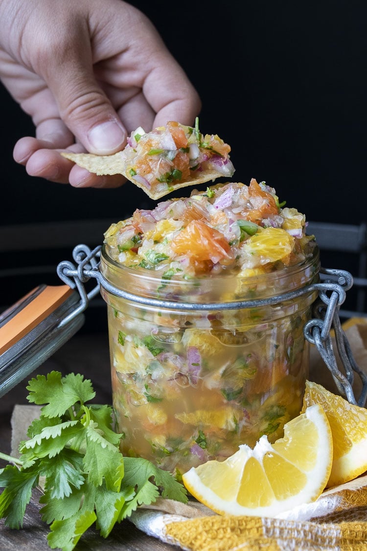 Hand dipping a chip into a glass jar filled with fresh citrus salsa